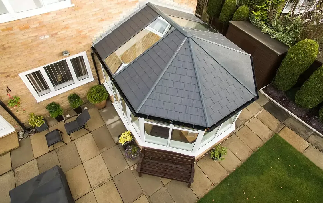 Aerial view of conservatory with grey tiled roof and roof windows, patio, and garden.